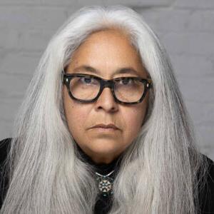 Laurie Steelink的肖像照. 斯蒂尔林克有一头又长又直的灰色头发，戴着黑色的上衣和黑框眼镜.